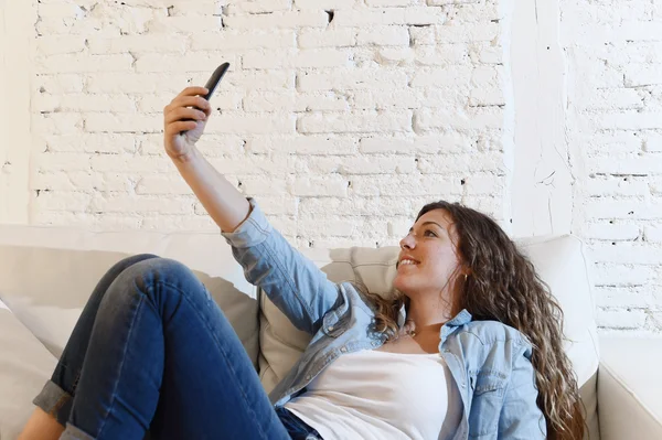 Young attractive hispanic woman lying on home couch taking selfie photo with mobile phone having fun — 图库照片