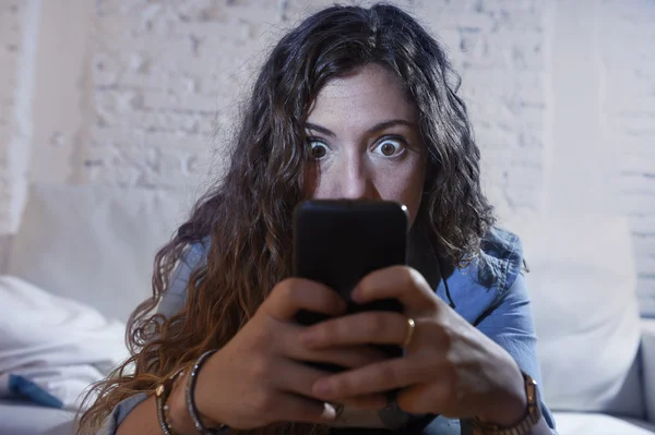 Hispanic woman holding mobile phone in crazy eyes social network and internet addiction concept — Stock Photo, Image