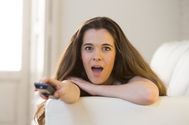 young beautiful woman lying on couch holding remote control watching television happy