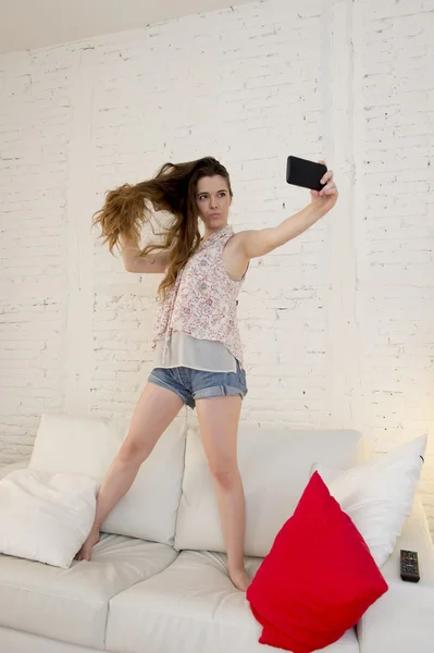 Felice ragazza attraente che gioca sul divano di casa prendendo selfie ritratto con il telefono cellulare divertirsi — Foto Stock