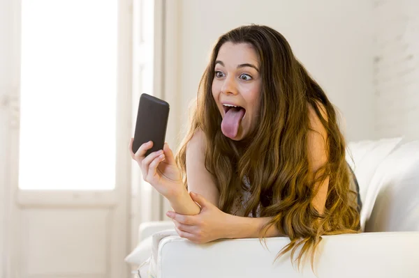 Feliz chica atractiva jugando en el sofá de casa tomando retrato selfie con el teléfono móvil divertirse — Foto de Stock