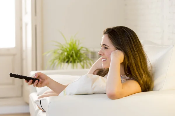 Joven hermosa mujer acostada en sofá celebración de control remoto viendo la televisión feliz y relajado — Foto de Stock