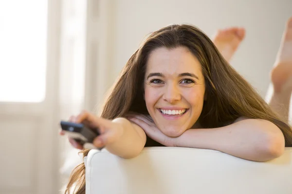 Joven hermosa mujer acostada en sofá celebración de control remoto viendo la televisión feliz y relajado —  Fotos de Stock