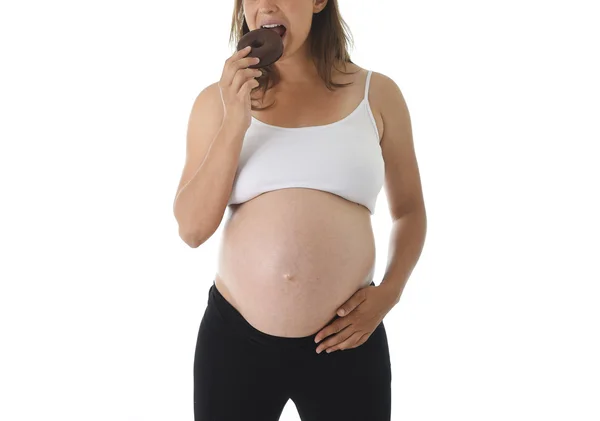 Büyük beline eliyle tutarak ve çikolatalı çörek yiyen genç çekici hamile kadın — Stok fotoğraf