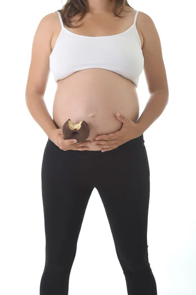 Joven atractiva embarazada sosteniendo su gran vientre con la mano y comiendo donut de chocolate — Foto de Stock
