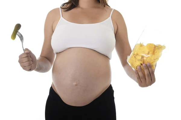 Jovem mulher grávida atraente mostrando barriga grande comer chips segurando pickle com garfo — Fotografia de Stock