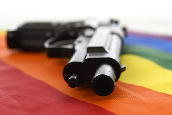 Nature morte avec gros plan pistolet reposant sur le drapeau gay défilé représentant la discrimination sexuelle et l'intolérance — Photo