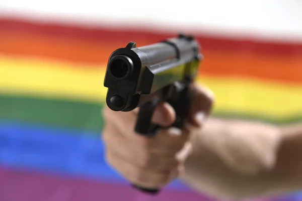 Homme tenant pistolet de près avec fond gay défilé drapeau représentant la discrimination sexuelle — Photo