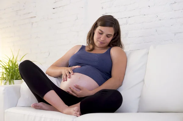 Muda cantik bahagia 8 atau 9 bulan wanita hamil di rumah ruang tidur sofa memegang perut besar — Stok Foto