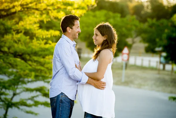 Lyckliga par i kärlek tillsammans i parkera landskap på solnedgången med kvinna gravid mage och man — Stockfoto