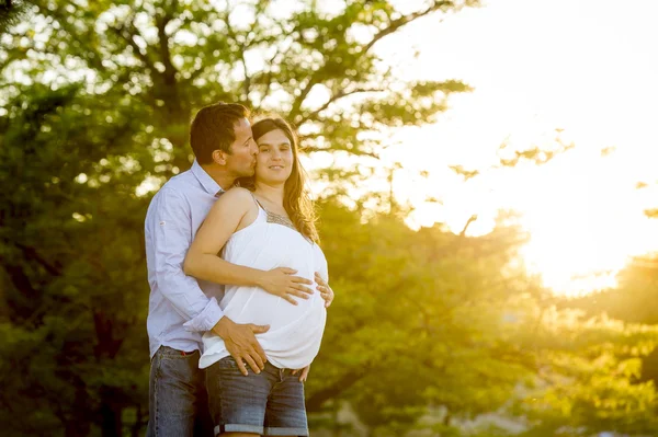 Aşık kadın hamile karnına ve adam Sunset'teki park peyzaj birlikte mutlu çift — Stok fotoğraf