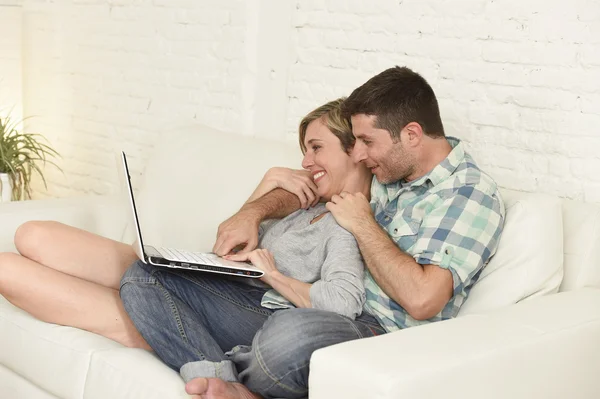 Belo casal apaixonado no sofá, juntamente com computador portátil feliz em casa usando a internet — Fotografia de Stock