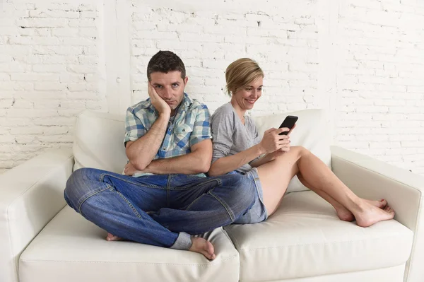 Ελκυστικό ζευγάρι στο σπίτι καναπές ευτυχισμένη γυναίκα εθισμένος στο διαδίκτυο στο κινητό τηλέφωνο αγνοώντας λυπημένος σύζυγος — Φωτογραφία Αρχείου
