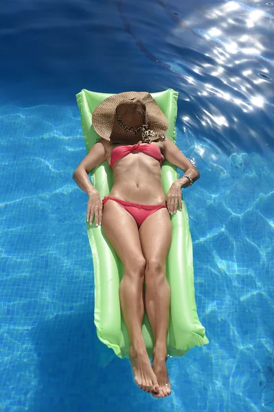 Счастливая красивая женщина в бикини и солнцезащитной шляпе, лежащая на плавучей кровати в бассейне курортного отеля — стоковое фото