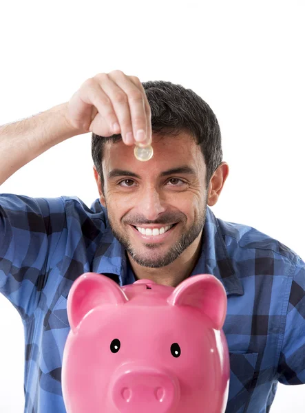 Jovem homem feliz segurando moeda colocá-lo em rosa porquinho banco — Fotografia de Stock