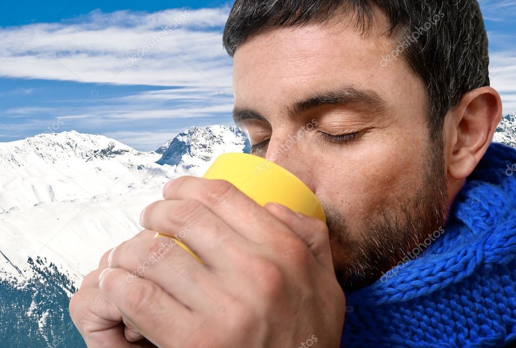 Young attractive man outdoors drinking cup of coffee or tea in cold winter snow mountain at xmas holiday