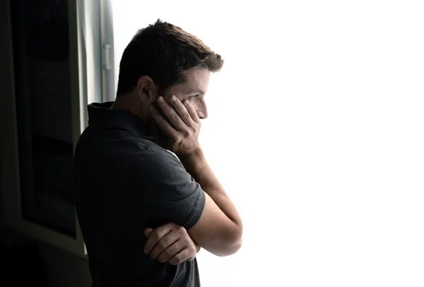 Atractivo hombre mirando a través de la ventana sufriendo crisis emocionales y depresión —  Fotos de Stock