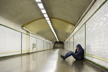 Young man lost in depression sitting on ground street subway tunnel clipart