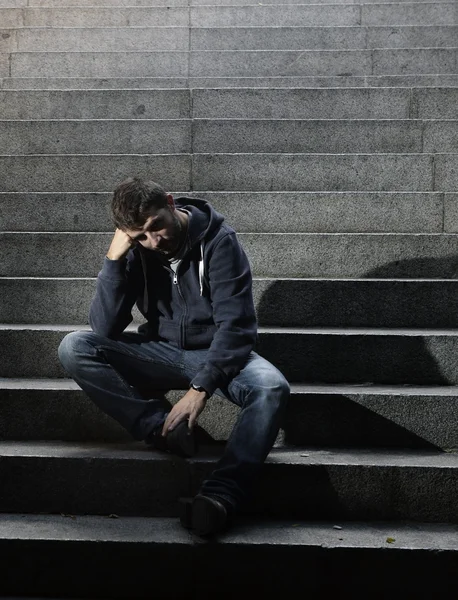 Молодой человек, потерявшийся в депрессии, сидит на бетонной лестнице — стоковое фото
