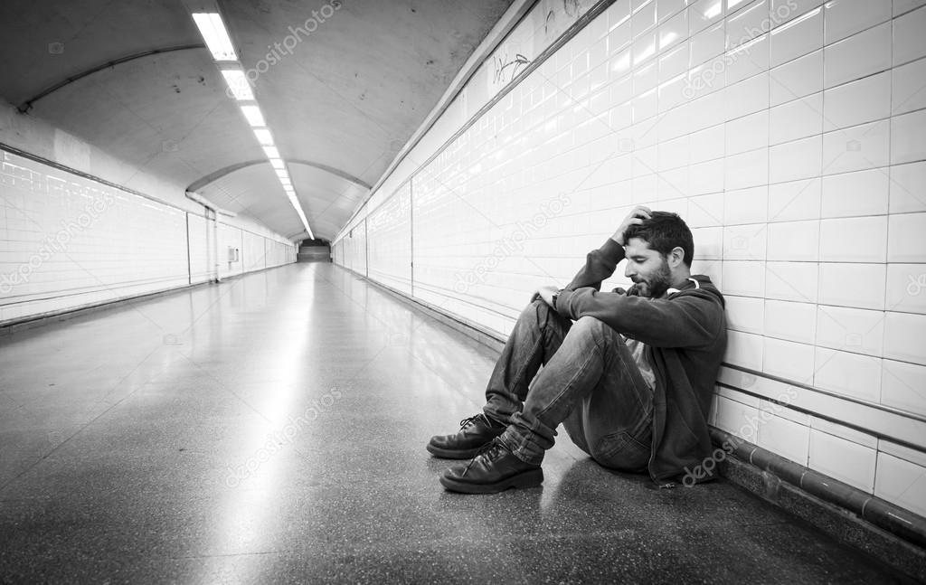 Young man lost in depression sitting on ground street subway tunnel