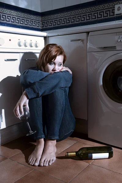 Eenzame dronken alcoholische vrouw zittend op de keukenvloer in depressie drinken van wijn — Stockfoto