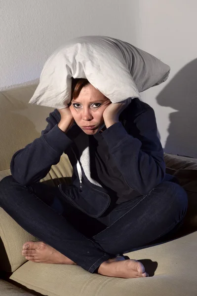 Woman sitting on couch holding pillow against head in stress and depression — Stock Photo, Image