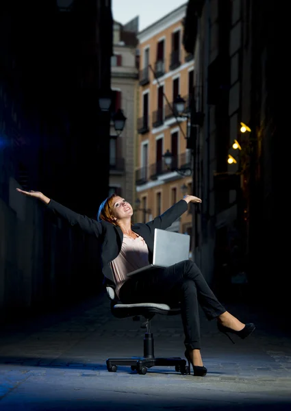 Unga glada affärskvinna som sitter på kontorsstol på gatan med laptop — Stockfoto