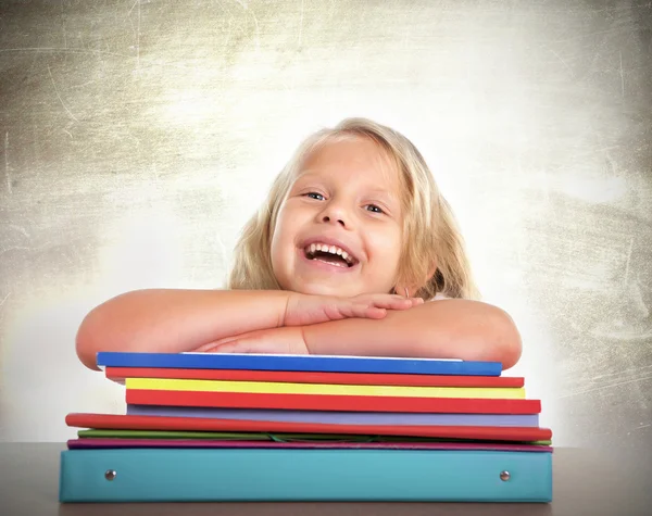 Nettes Schulmädchen mit blonden Haaren sitzt glücklich auf dem Schreibtisch und lächelt — Stockfoto