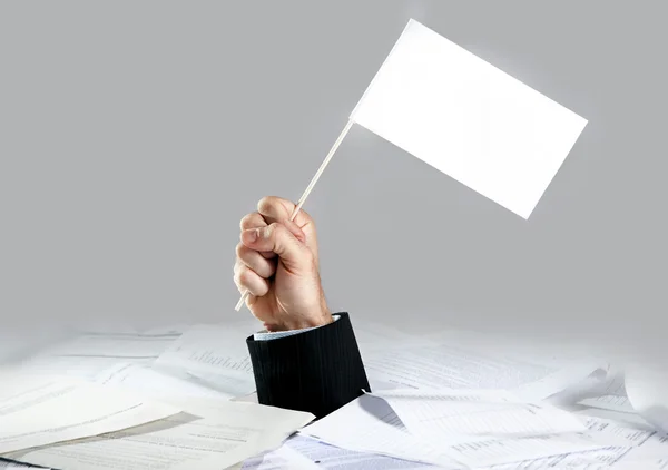 Hand van zakenman opkomende van geladen papierwerk Bureau houden witte vlag — Stockfoto