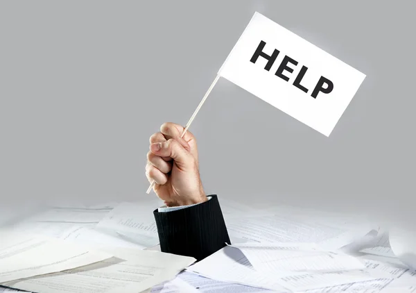 Hand of  businessman emerging from loaded paperwork desk holding white flag asking for help — Stock Photo, Image