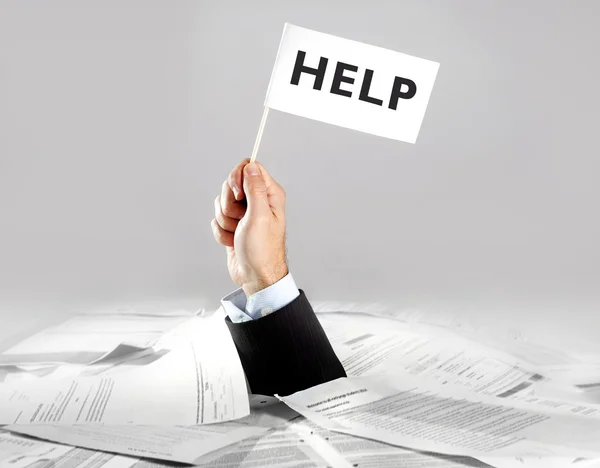 Hand of  businessman emerging from loaded paperwork desk holding white flag — Stock Photo, Image