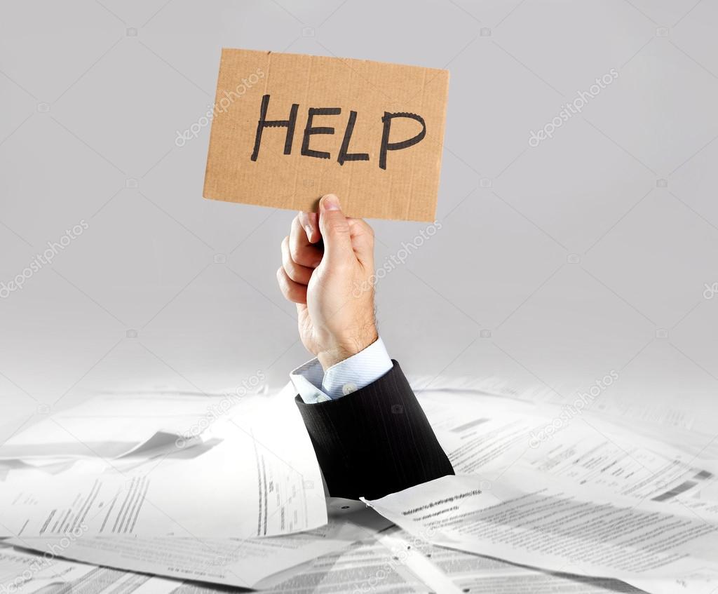 Hand of  businessman emerging from loaded paperwork desk holding help message