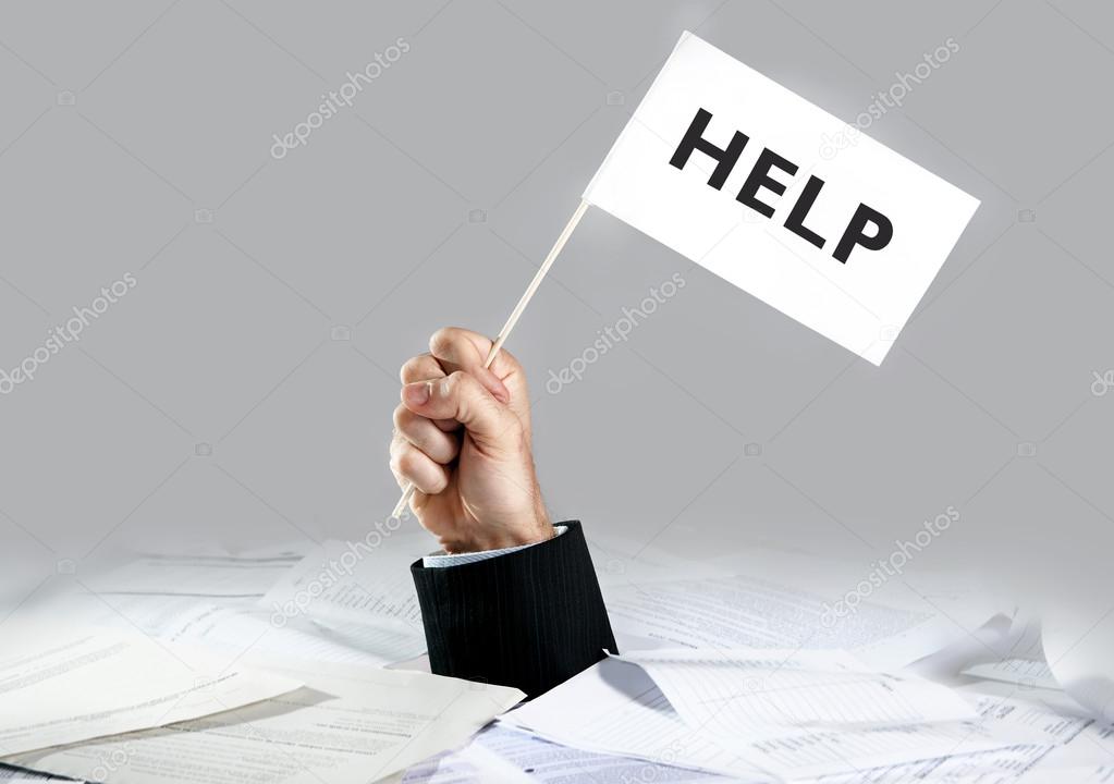 Hand of  businessman emerging from loaded paperwork desk holding white flag asking for help