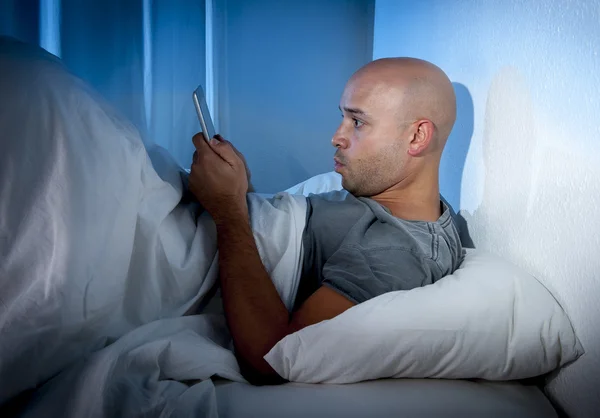 Young internet addict man awake at night in bed using digital pad or tablet