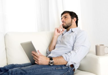 Genç çekici İspanyol adam evde beyaz kanepede dijital tablet veya pad kullanarak