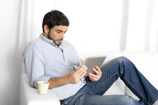 Giovane uomo ispanico attraente a casa sul divano bianco utilizzando tablet o pad digitale — Foto Stock