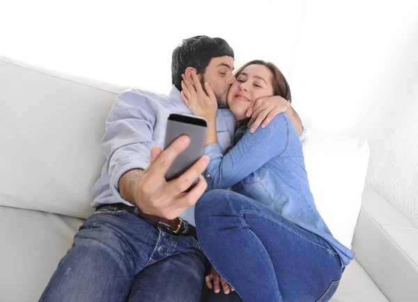 Nice attractive young couple sitting together in sofa couch taking selfie photo with mobile phone — Stock Photo, Image