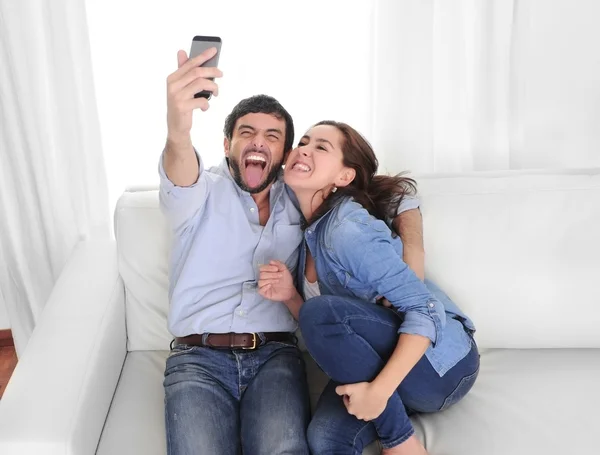 Nice attractive young couple sitting together in sofa couch taking selfie photo with mobile phone — Stock Photo, Image
