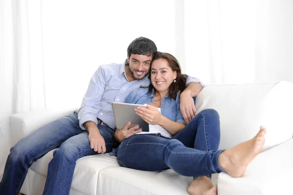 Jovem casal feliz no sofá em casa gostando de usar o computador tablet digital — Fotografia de Stock