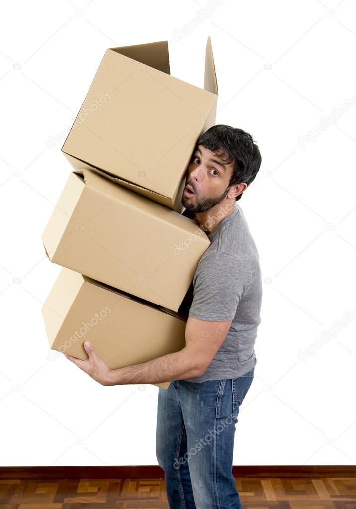 young man moving in a new house carrying pile of cardboard boxes 