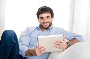 Genç çekici İspanyol adam evde beyaz kanepede dijital tablet veya pad kullanarak