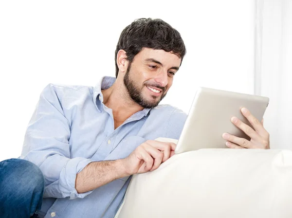 Young attractive Hispanic man at home on white couch using digital tablet or pad — Stock Photo, Image