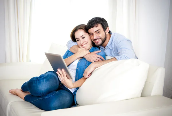 Jovem casal feliz no sofá em casa gostando de usar o computador tablet digital — Fotografia de Stock
