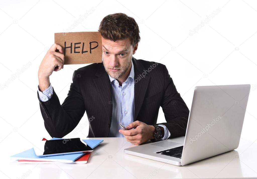 attractive businessman working in stress at computer holding help cardboard sign