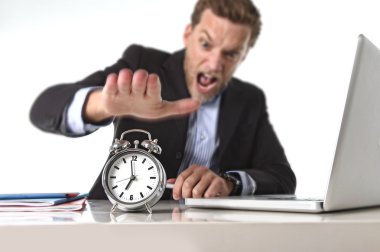 Exploited businessman at office desk stressed and frustrated with  alarm clock in out of time and deadline concept clipart
