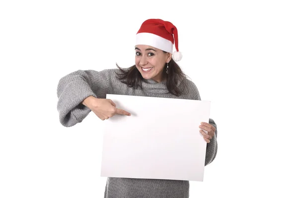 Joven dulce latina mujer en santa navidad sombrero apuntando en blanco cartelera —  Fotos de Stock