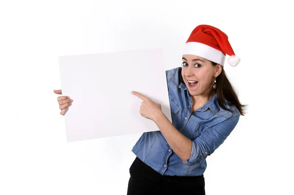 Joven dulce latina mujer en santa navidad sombrero apuntando en blanco cartelera —  Fotos de Stock