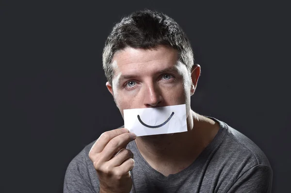 Jeune homme déprimé perdu dans la tristesse et le chagrin tenant papier avec le sourire sur sa bouche dans la dépression concept — Photo