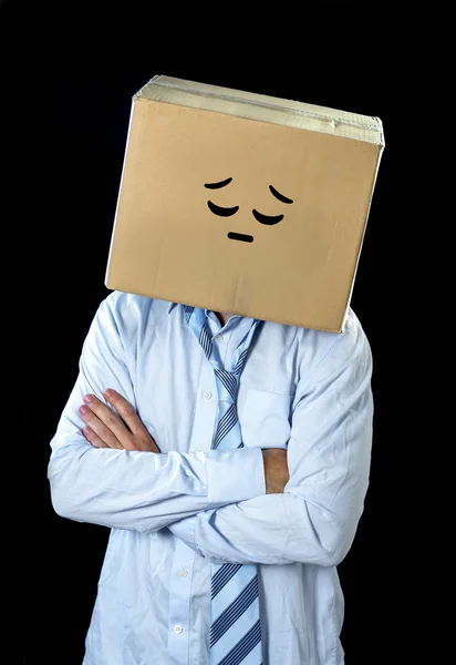 Λυπημένος και κατάθλιψη επιχειρηματίας φορώντας γελοιογραφία χαμογελαστό πρόσωπο ζωγραφισμένο σε κουτί από χαρτόνι πάνω από το κεφάλι — Φωτογραφία Αρχείου