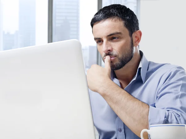 Attraente uomo d'affari che lavora al computer alla scrivania dell'ufficio di fronte alla finestra del grattacielo — Foto Stock